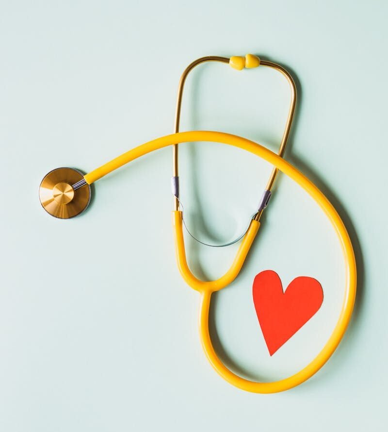 Yellow stethoscope arranged with a red heart cutout on a light green background, symbolizing heart health.
